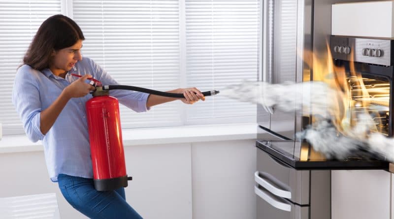 Woman Putting Out Fire in Oven With Extinguisher