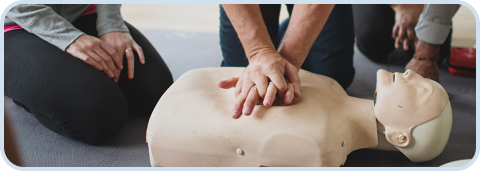 Two hands delivering chest compressions on a CPR training mannequin during a CPR class.